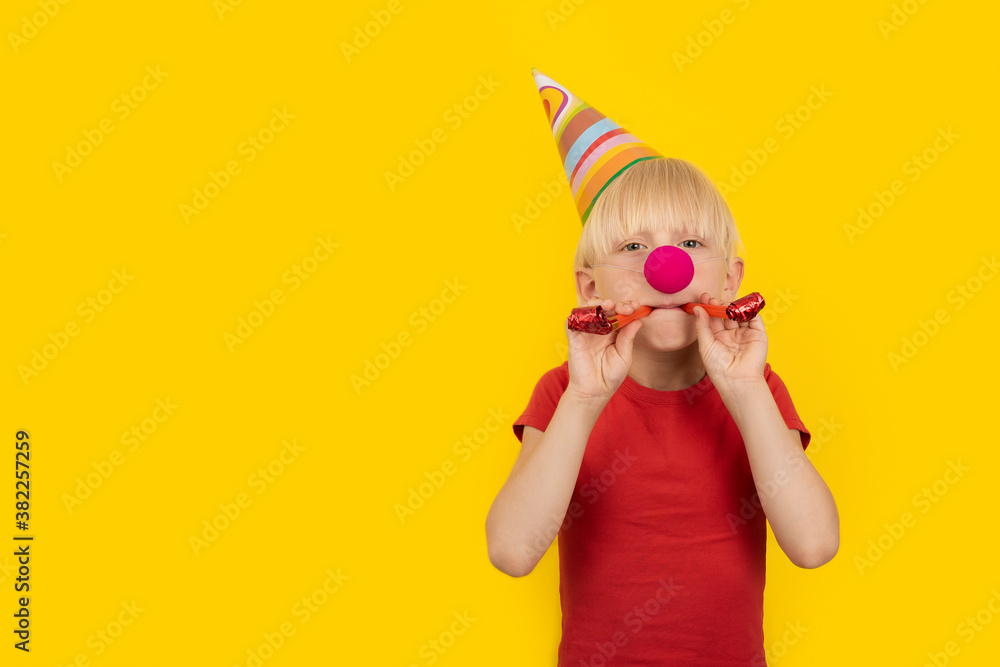 Boy with party hat and red clown nose holding whistle. Portrait on yellow background. Holiday matinee Boy with party hat and red clown nose holding whistle. Portrait on yellow background. Holiday matinee
