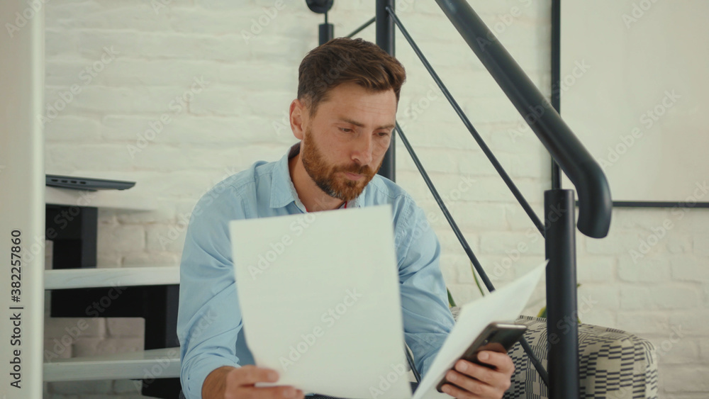 Fototapeta premium Unhappy businessman working with smartphone and documents on sofa holds papers worried sad phone smartphone internet cell attractive slow motion