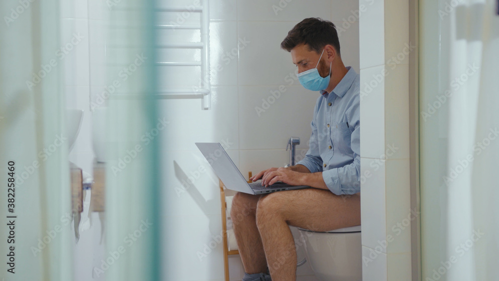 Happy businessman working on laptop wearing mask sit on the toilet at home restroom bearded funny wc isolation quarantine pandemic coronavirus covid-19 portrait close up slow motion