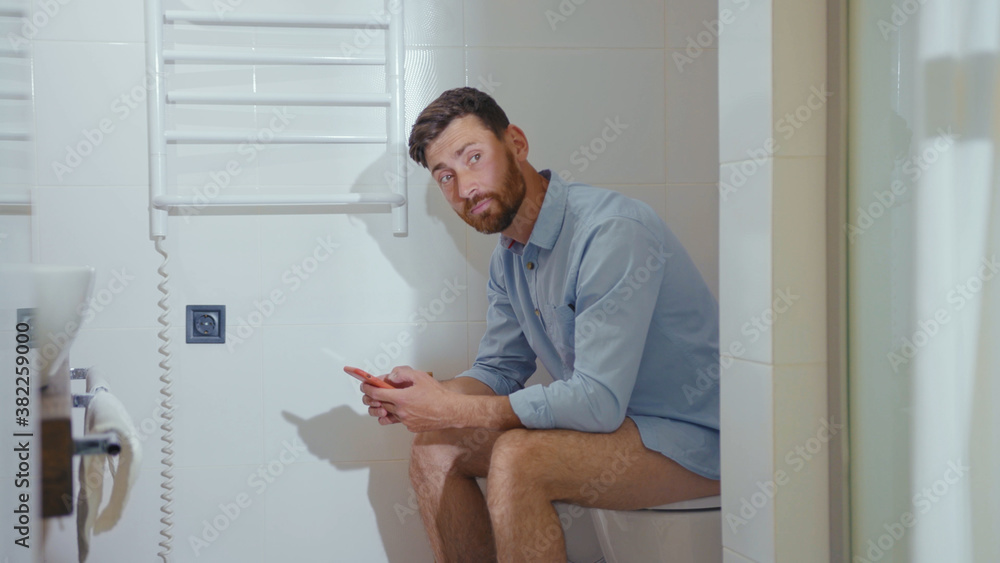 Happy businessman use phone sitting on the toilet smiling mobile restroom smartphone internet home bathroom close up slow motion