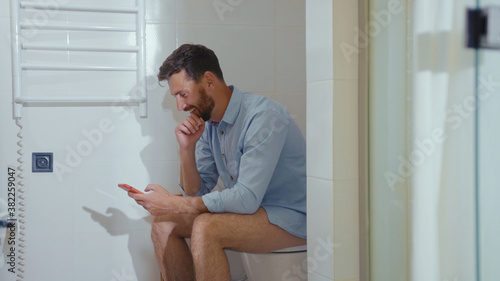 Happy businessman use phone sitting on the toilet smiling mobile restroom smartphone internet home bathroom close up slow motion