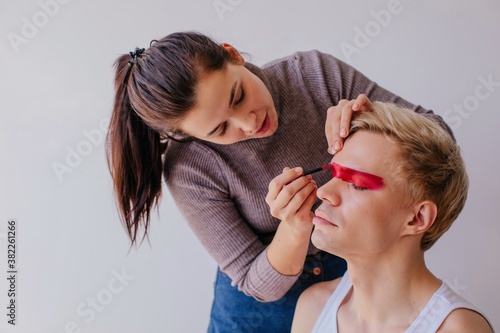 Female visagiste applying makeup on male model photo