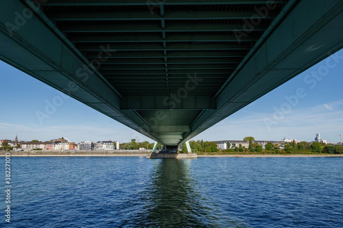 Outdoor sunny view on riverside of Rhine river under Deutzer Brücke, suspension green bridge, in Cologne, Germany. © Peeradontax