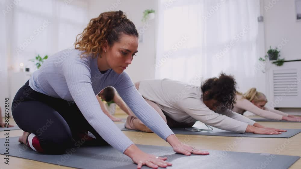 Group on exercise mats stretching in yoga class inside community center - shot in slow motion Group on exercise mats stretching in yoga class inside community center - shot in slow motion