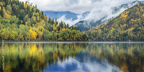 Reflection in the water of the mountains and sky. The calm flow of the Yenisei River in Siberia. Autumn view.