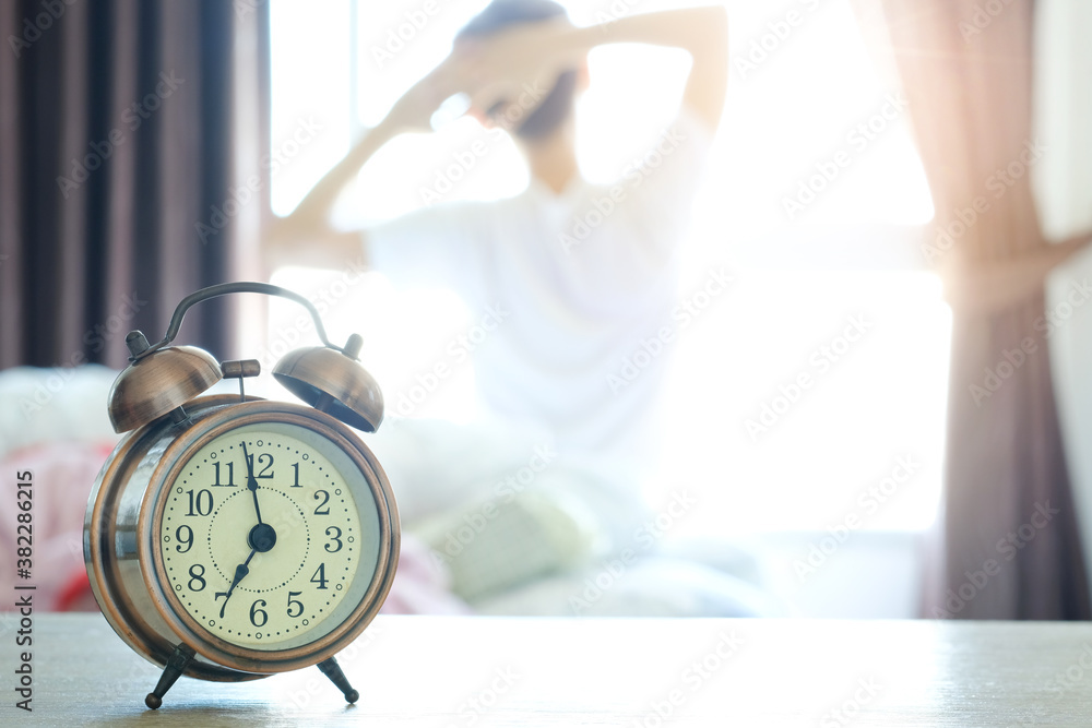 © Photo Sesaon - Morning of a new day, alarm clock wake up woman sitting in the room. A woman stretch the muscles at window. Health and care concepts