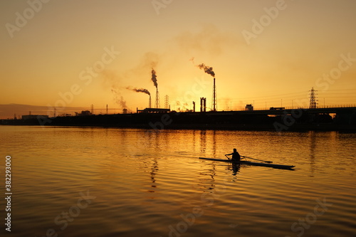 夕方の工業地帯の運河で練習するボート競技者