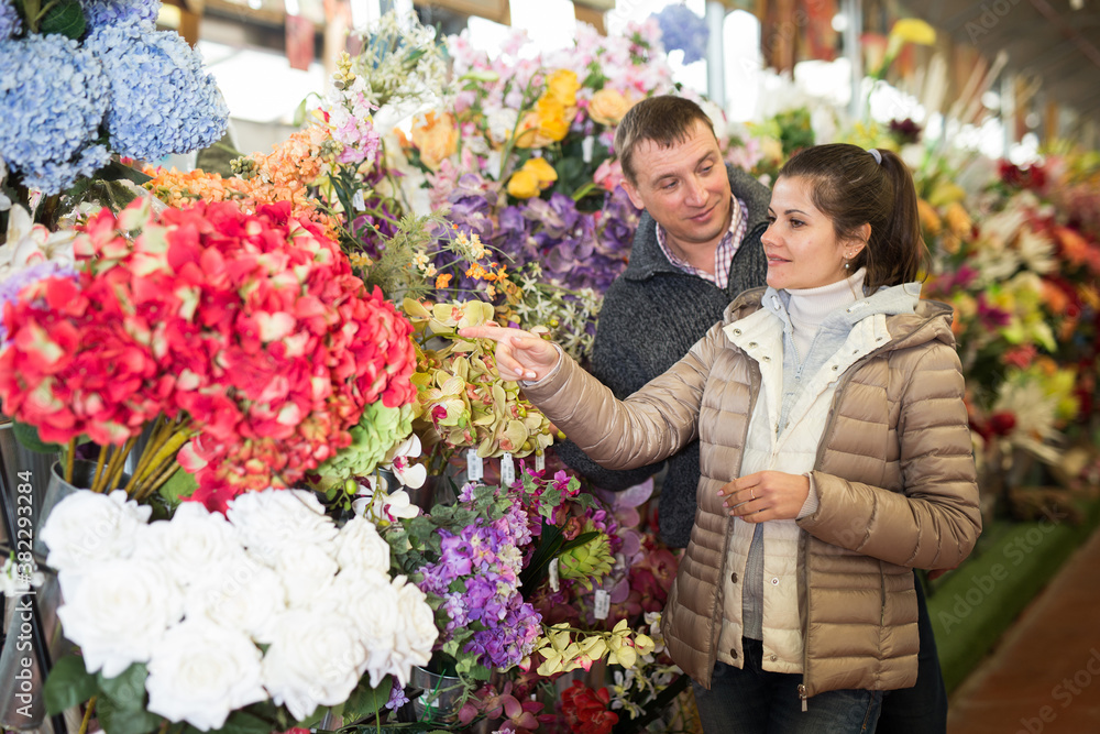Portrait of young man and woman choosing together bouquet at flowers shop