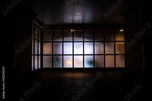 Frosted glass wall with black metal frame in grid pattern with bright light from the inside looking from the hallway. 