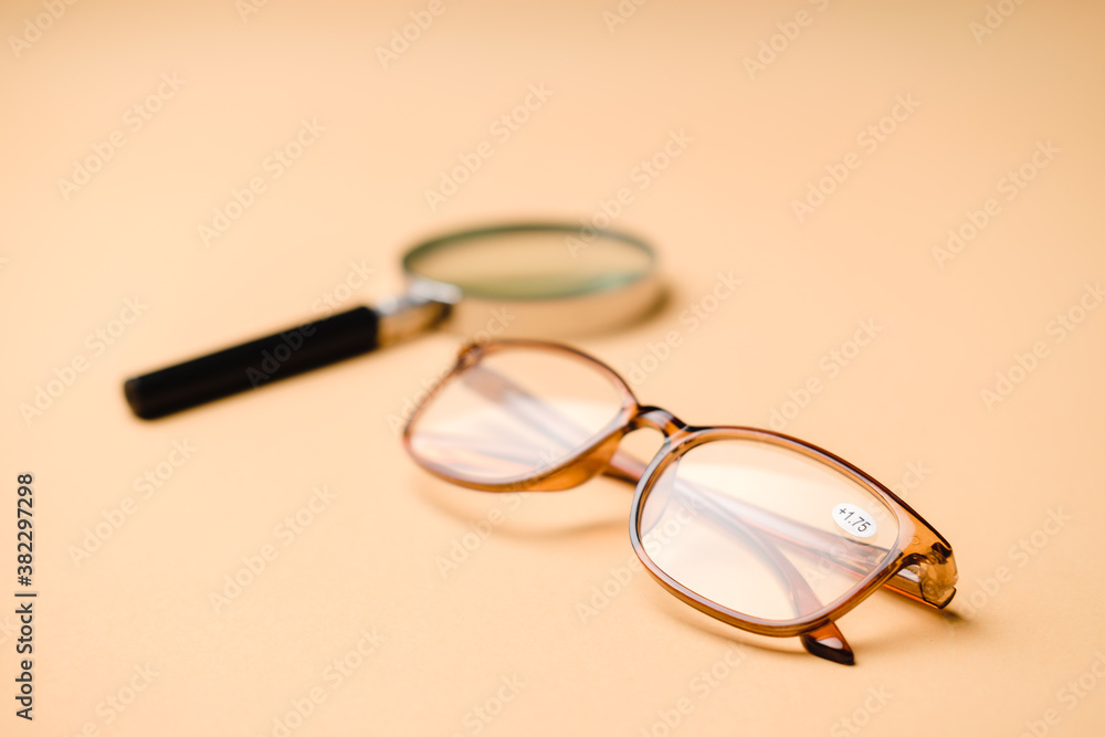 Orange eyeglasses for farsighted people with magnifying glass on an orange pastel background. Orange eyeglasses for farsighted people with magnifying glass on an orange pastel background.