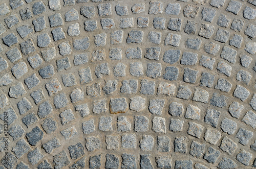 A fragment of pavement paved with rough square gray stone blocks with uneven edges in the form of semicircular arched streaks.