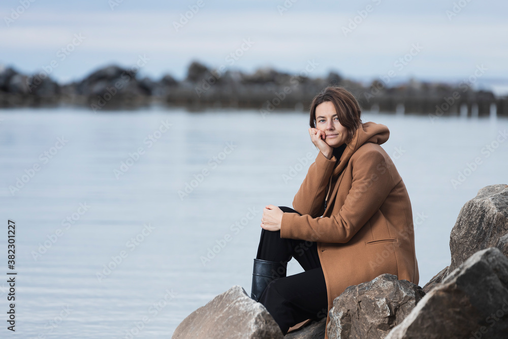 Fashion lifestyle portrait of young trendy woman dressed in  a beige wool coat smiling, walking on the beach,  on background a sea .Portrait of joyful woman