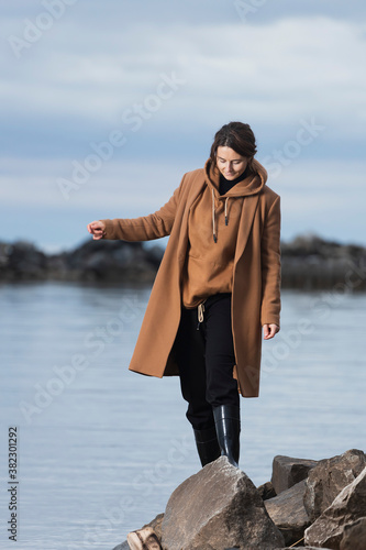 A romantic walk of a curly-haired woman in  beige wool coat   posing on stone in sea. The concept of female freedom, emancipation and love © Виталий Сова