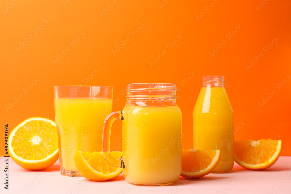 Glass jars with orange juice on pink table Glass jars with orange juice on pink table