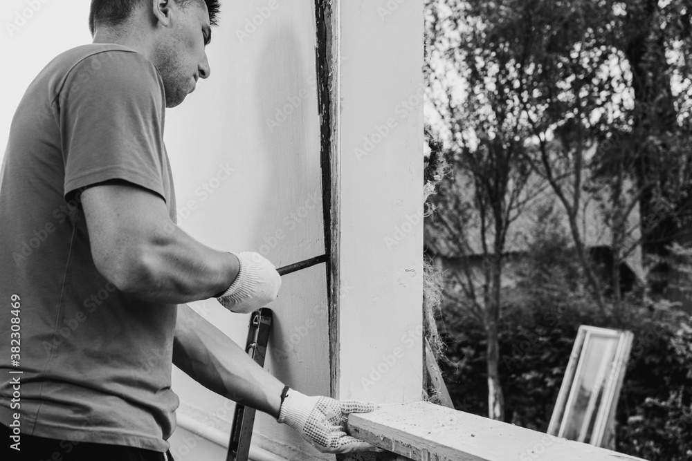 Fototapeta premium the master dismantles the old window with a crowbar, weighs the old window frame from the wall with a crowbar, performs dismantling work.