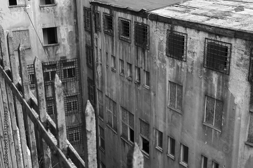 Old abandoned communist prison with broken windows and rusty secured grills, scary landmark black and white photo