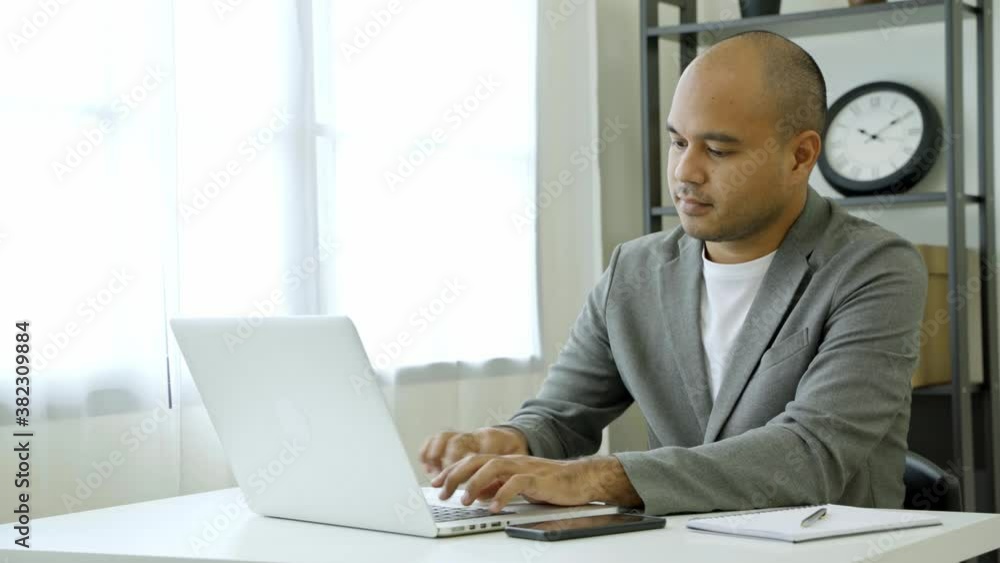 Work from home concept. Asian male business wear a suit work and typing with laptop stop to use mobile phone to talk and sit at home office desk. 4K Resolution. Work from home concept. Asian male business wear a suit work and typing with laptop stop to use mobile phone to talk and sit at home office desk. 4K Resolution.