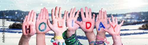 Children Hands Building Colorful English Word Holiday. Snowy Winter Background With Snowflakes