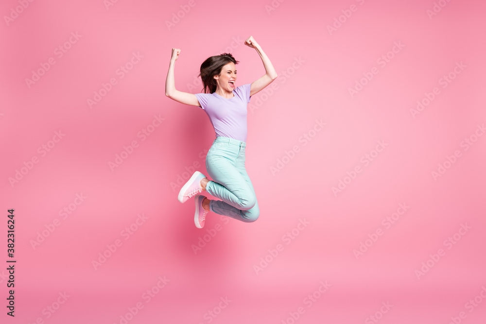 Full size photo of delighted crazy girl jump enjoy lottery win raise fists scream wear turquoise violet trousers sneakers isolated over pastel color background