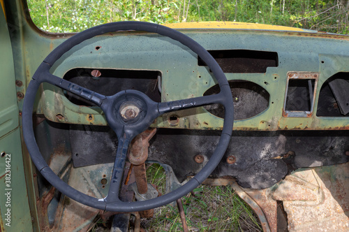 Interior of an antique car with a steering wheel and missing floorboard