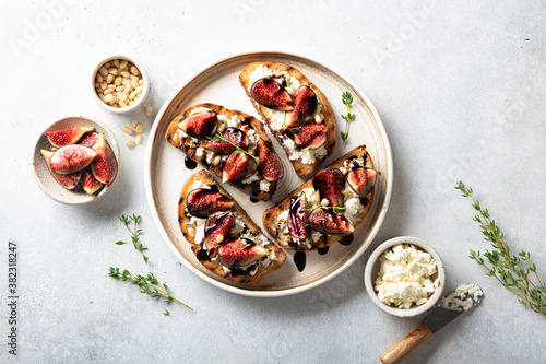 bruschetta with figs, cream cheese, balsamic sauce and pine nuts in a ceramic plate on a light background, top view