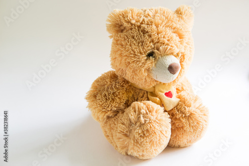 Soft Teddy bear with long light brown fur and a red heart on a scarf around his neck. Valentine's day gift, children's toy. White background, space for text