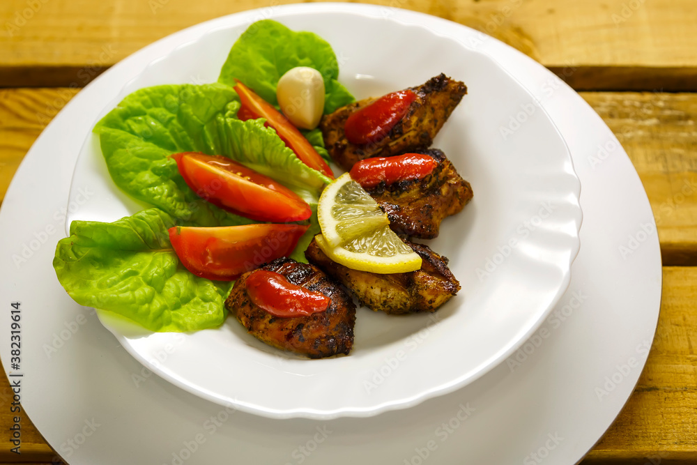 Pieces of grilled meat with tomato, salad and lemon are laid out on a plate. Pieces of grilled meat with tomato, salad and lemon are laid out on a plate.