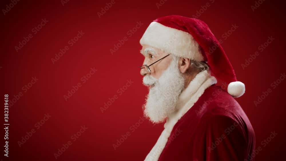 Medium shot portrait of slinking Santa Claus appearing against red background, looking at camera, getting scared and going away Medium shot portrait of slinking Santa Claus appearing against red background, looking at camera, getting scared and going away