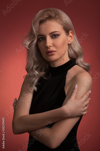 Beautiful blonde girl with exquisite makeup and long legs in a black dress on a red background