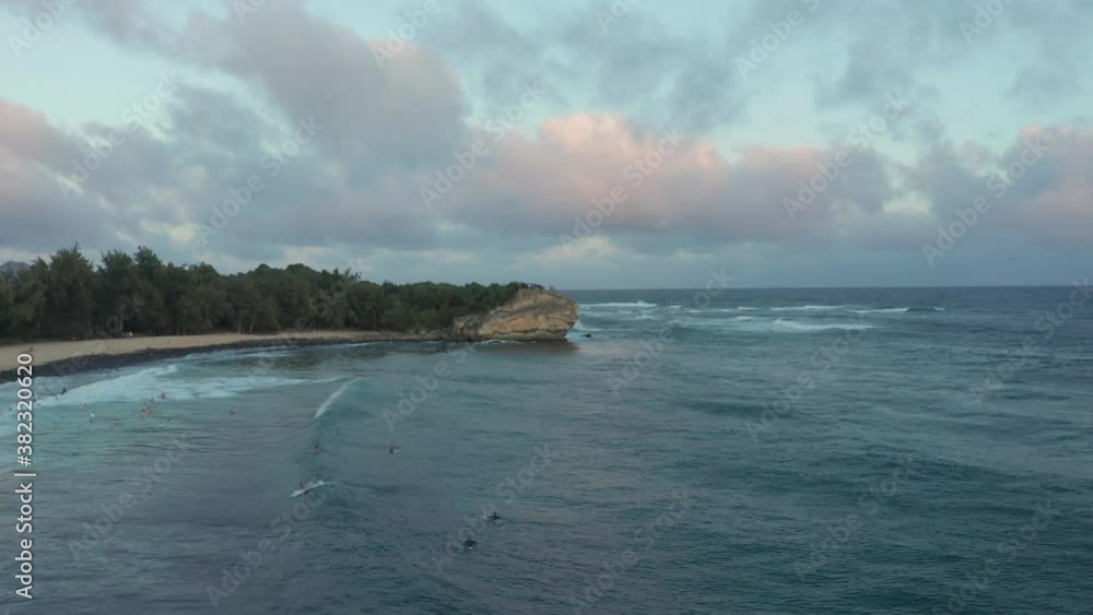 Surfers at sunset in Hawaii drone shot over the waves overlooking bay and beach. Slow motion aerial view flying backwards revealing surfing spot. Poipu Kauai Surfers at sunset in Hawaii drone shot over the waves overlooking bay and beach. Slow motion aerial view flying backwards revealing surfing spot. Poipu Kauai