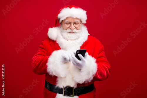 Portrait of his he nice attractive handsome cheerful focused Santa father using device gadget 5g web service blog post smm comment isolated over bright vivid shine vibrant red color background