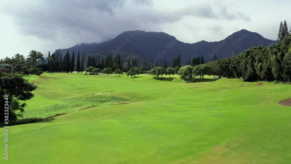 Tropical Golf Course Green and bunker sand trap in aerial drone shot low angle. Mountains in background on sunny and cloudy day in golfers paradise Tropical Golf Course Green and bunker sand trap in aerial drone shot low angle. Mountains in background on sunny and cloudy day in golfers paradise