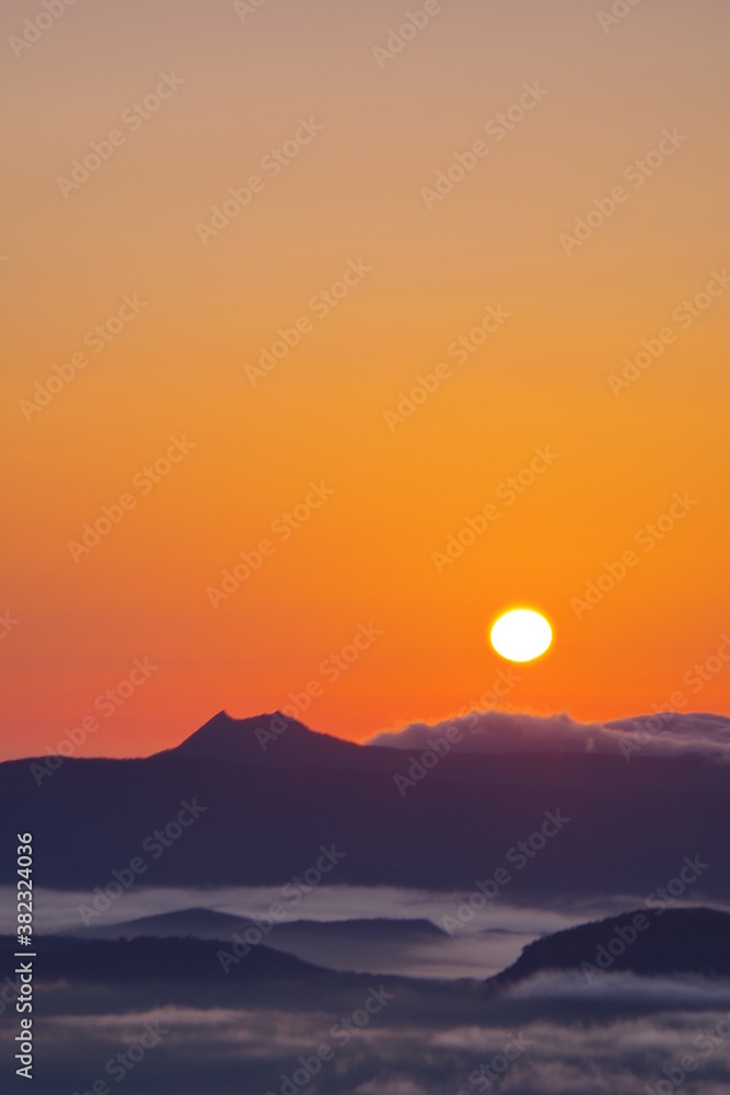 夜明けの太陽と朝靄の漂う大地、山々のシルエット。北海道、津別峠からの風景。