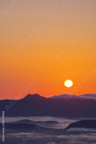夜明けの太陽と朝靄の漂う大地、山々のシルエット。北海道、津別峠からの風景。