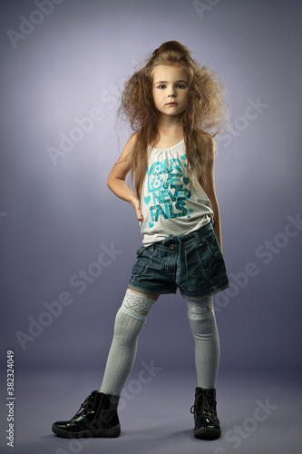 Beautiful girl blonde child schoolgirl in a T-shirt denim shorts and socks with stylish hairstyles on a white background