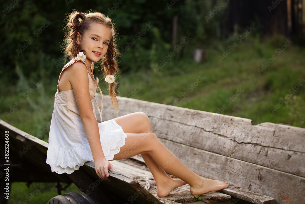 Beautiful blonde child girl in a white dress sits on an old rustic cart Beautiful blonde child girl in a white dress sits on an old rustic cart
