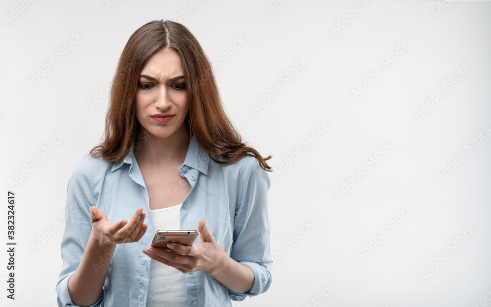 Indignant Young woman holds the smartphone in her hand. She doesn't understand how to use the new app