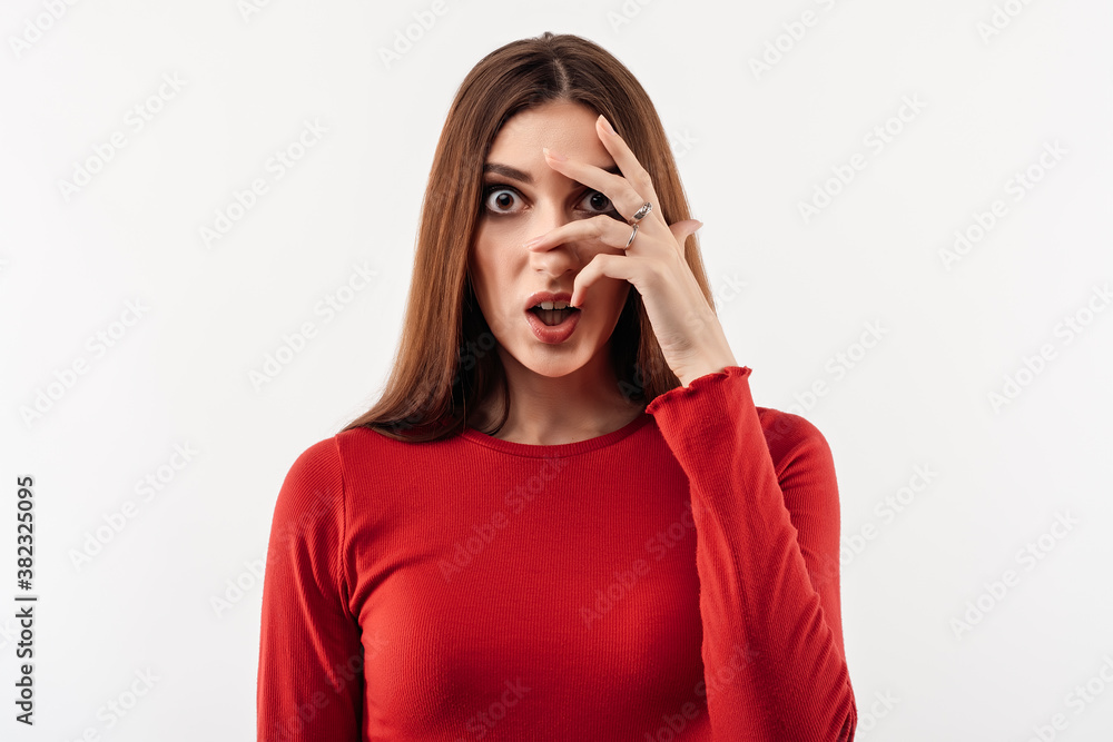 Portrait of frightened young woman with long chestnut hair in casual red sweater covering her eyes with hands Portrait of frightened young woman with long chestnut hair in casual red sweater covering her eyes with hands