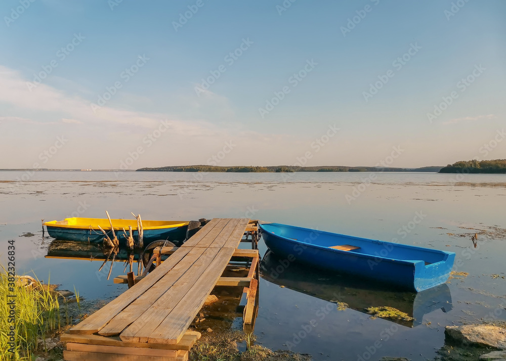 Yellow and blue boat in wooden pier on the lake calm summer evening