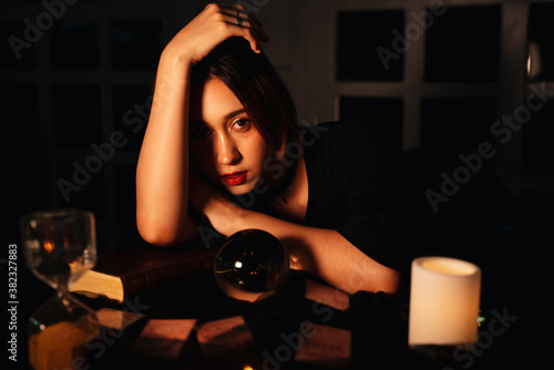 Beautiful young long hair woman fortune teller with crystal ball in dark room.
