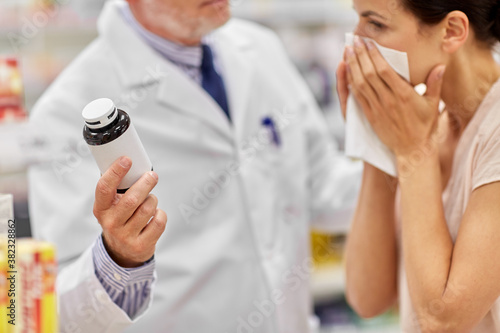 medicine, healthcare and people concept - senior apothecary shows drug to ill woman at pharmacy