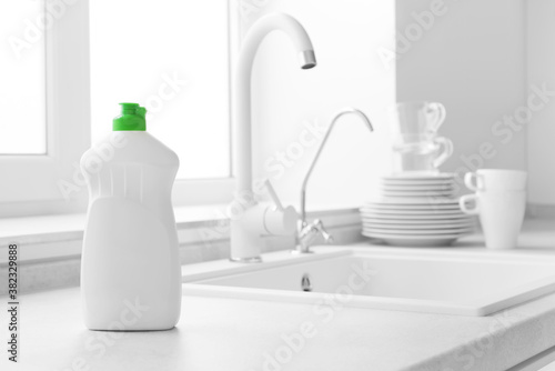 Dishwashing liquid bottle on kitchen sink and clean plates background photo