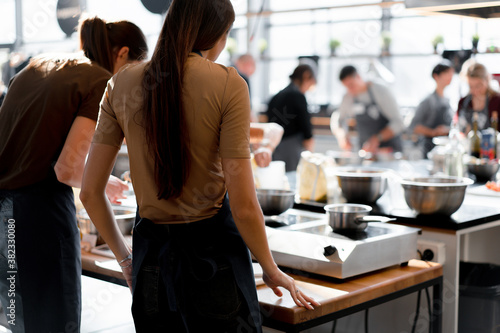 Culinary class. Back view of the process of cooking. Different unrecognizable people in gray apronsthe in the kitchen learn to cook photo