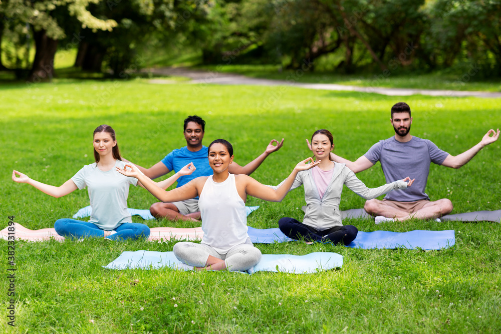 fitness, sport, yoga and healthy lifestyle concept - group of happy people meditating in lotus pose at summer park fitness, sport, yoga and healthy lifestyle concept - group of happy people meditating in lotus pose at summer park