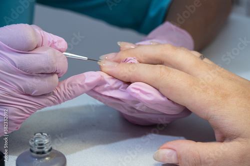 The process of hardware manicure. Alignment of the base transparent nail Polish on the hands with a thin brush.