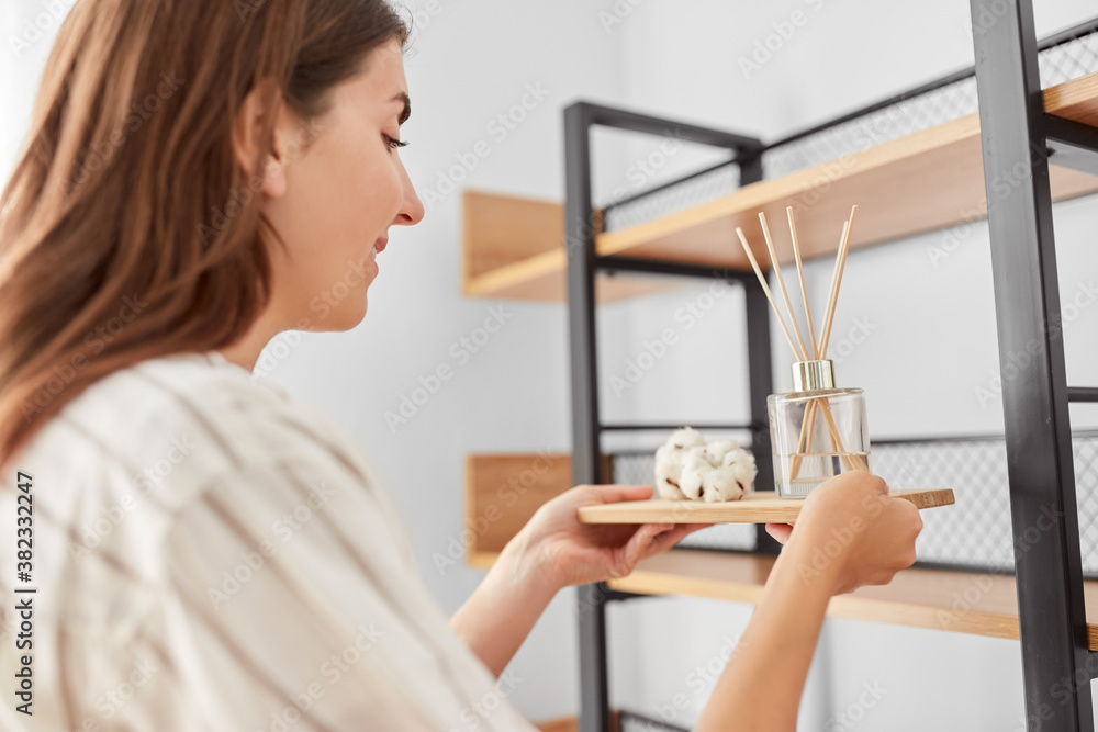 home improvement, decoration and people concept - happy smiling woman placing aroma reed diffuser to shelf - obrazy, fototapety, plakaty 