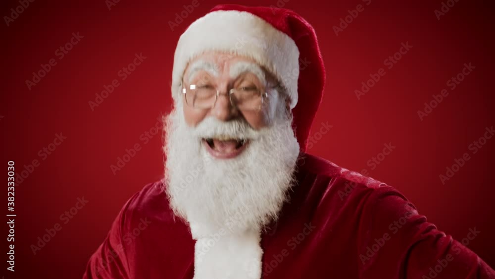 Lockdown portrait of Santa Claus looking at camera and laughing loudly while standing against red wall Lockdown portrait of Santa Claus looking at camera and laughing loudly while standing against red wall