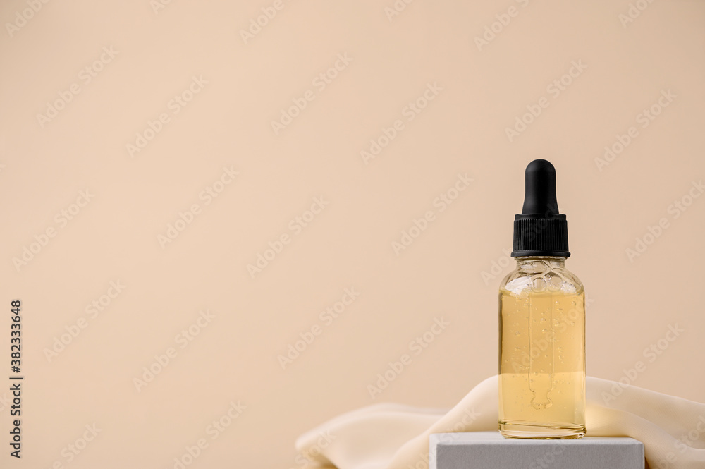 Naklejka premium Serum in a glass bottle with a pipette on a gray stand with a silk cloth. Essential oil for the care of female skin. Skin care, moisturizing beauty product on a beige background. Copy space