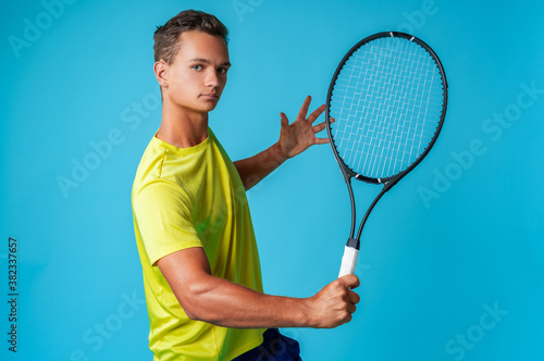 Young man tennis player in sportswear posing against blue background