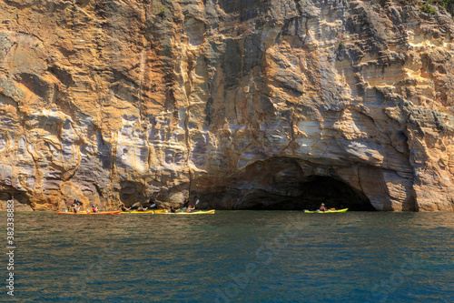 Kayakers passing in front of a sea cave in a steep cosatal cliff. Photographed near Hahei on the Coromandel Peninsula, New Zealand